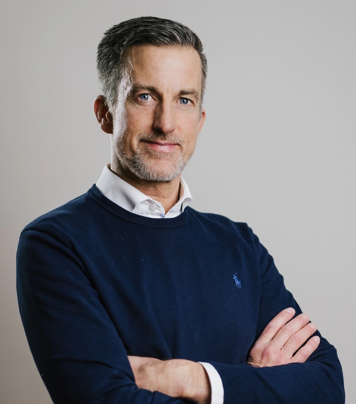 Porträt von Oliver Kober mit verschränkten Armen vor grauem Hintergrund – professionell, souverän und nahbar